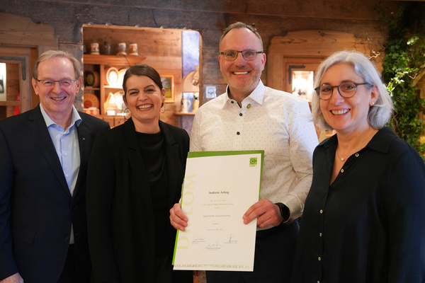 KI generiert: Eine Gruppe von vier Personen lächelt. Jemand hält ein Diplom. Text: „Andreas Arting, Diplomierte/r Gästeführerin“.