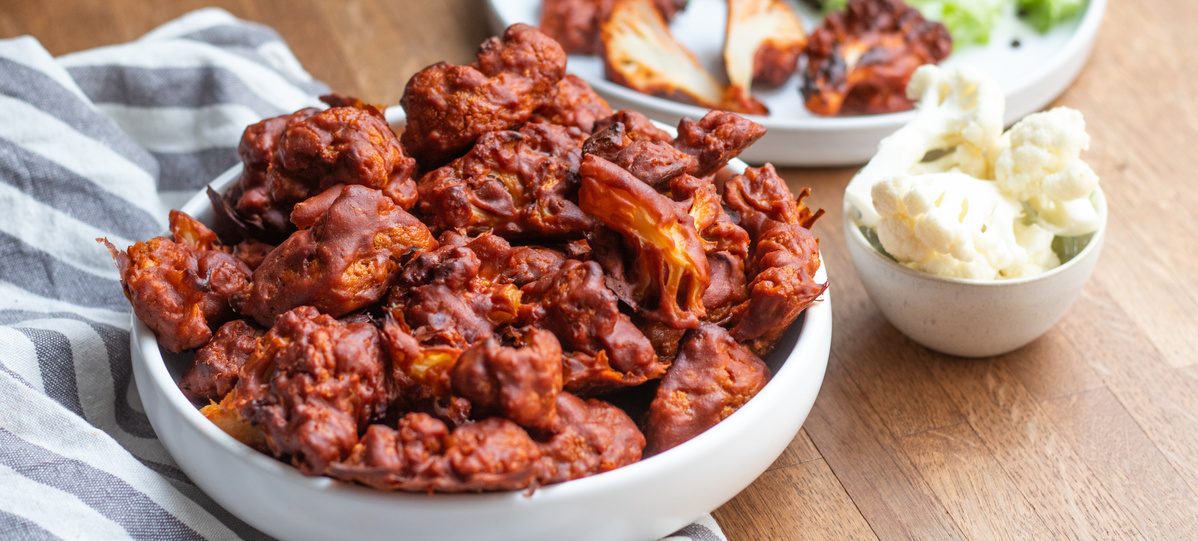 KI generiert: Ein Teller mit gebackenem Blumenkohl in würziger Sauce, daneben ein kleines Schälchen mit Dip.