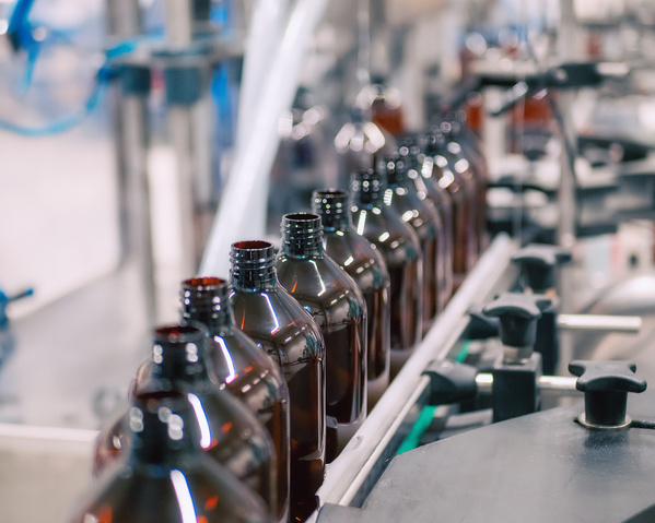 KI generiert: Reihe von braunen Flaschen auf einem Förderband in einer Produktionsanlage.