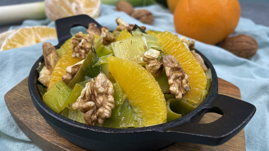 KI generiert: Das Bild zeigt eine Schale mit einem Salat aus Lauch, Orangen und Walnüssen, arrangiert auf einem Schneidebrett. Im Hintergrund sind eine Mandarine und eine Orange sichtbar.