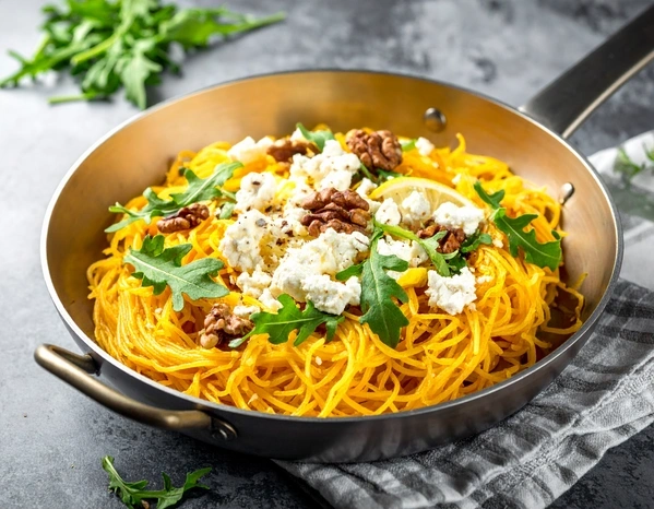KI generiert: Spaghetti-Kürbis mit Walnüssen, Rucola und Feta in einer Pfanne auf einem Tisch.