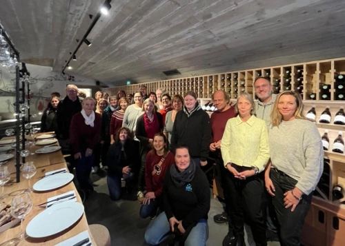 KI generiert: Eine Gruppe von Menschen posiert in einem Weinkeller mit gedecktem Tisch.