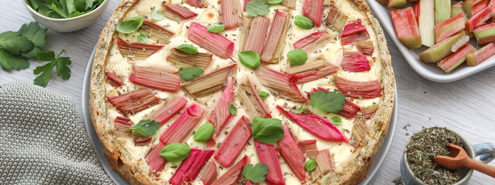 KI generiert: Eine Rhabarberquiche mit frischen Kräutern auf einem Tisch, daneben eine Schale mit Rhabarberstücken.
