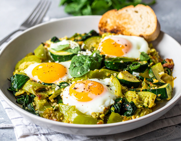 KI generiert: Das Bild zeigt gefüllte Champignons auf einem Holzbrett, garniert mit Käse und Kräutern. Im Hintergrund sind Zutaten wie Knoblauch, Nüsse und Öl zu sehen.
