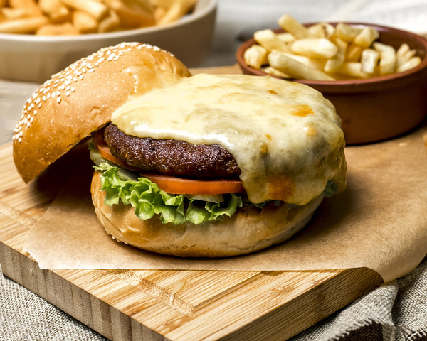 KI generiert: Ein Cheeseburger mit Salat und Tomaten, daneben eine Schale Pommes Frites.