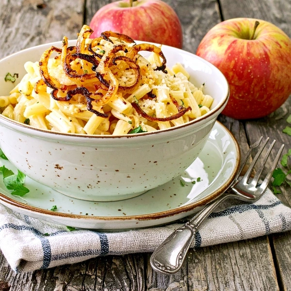 KI generiert: Ein Teller mit Käsespätzle und Röstzwiebeln, umgeben von Äpfeln auf einem Holztisch.