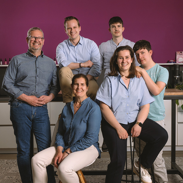 KI generiert: Eine Gruppe von sechs Personen lächelt vor einer violetten Wand in die Kamera.