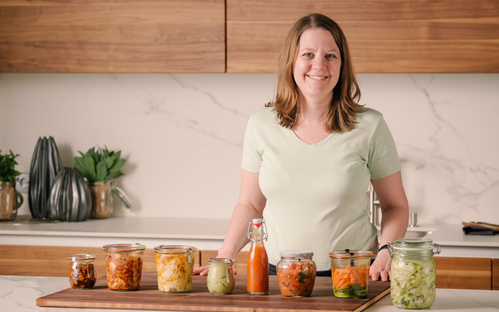 KI generiert: Eine Frau steht in einer Küche mit verschiedenen Konservengläsern vor sich.