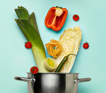 Unsere Kochboxen- Gemüse und Pasta ragen aus einem Kochtopf, auf blauem Hintergrund.