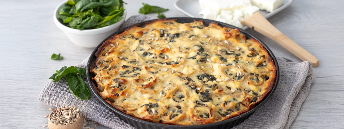 KI generiert: Ein gebackener Spinatquiche auf einem Küchentuch, daneben frischer Spinat und Käse.