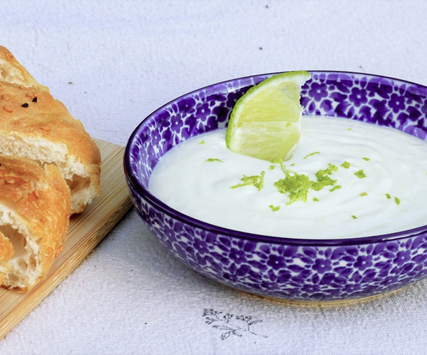 KI generiert: Ein Schälchen Joghurt-Mix mit Limette neben frischem Brot auf einem Brett.