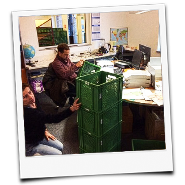 KI generiert: Personen in einem Büro stapeln grüne Kisten.