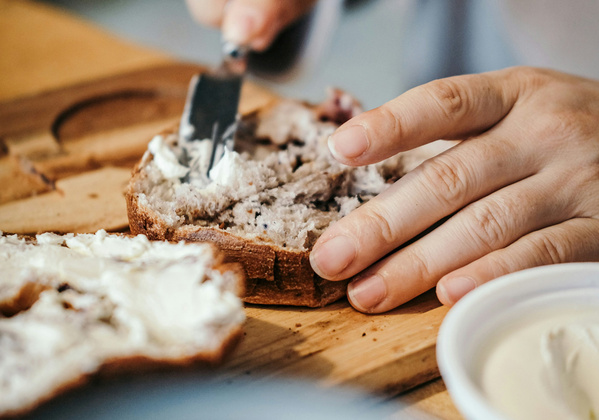 KI generiert: Eine Hand streicht Frischkäse auf ein Stück Brot.