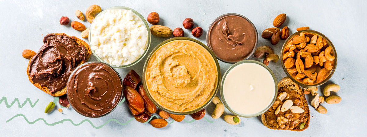 KI generiert: Verschiedene Nussmuse und Aufstriche in Schalen, umgeben von Nüssen und Brot.