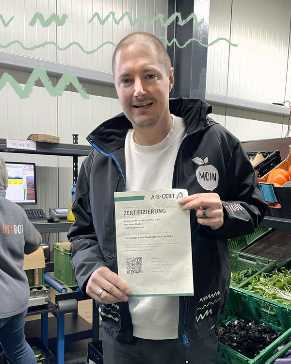 KI generiert: Mann hält Zertifikat für ökologischen Landbau in Lagerbereich. Text: "A·B·CERT ZERTIFIZIERUNG".