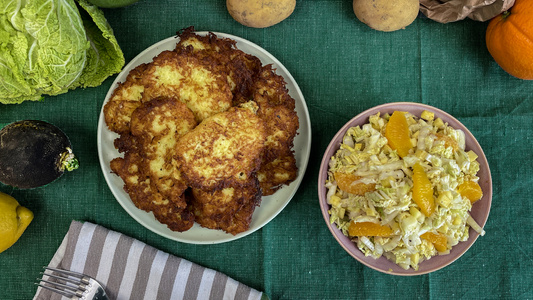 KI generiert: Das Bild zeigt eine Pfanne mit gebratenem Gemüse und Kartoffeln, gewürzt mit frischen Kräutern. Daneben sind Tomaten, Zucchini, Gewürze und weitere Zutaten auf einem Tisch platziert.