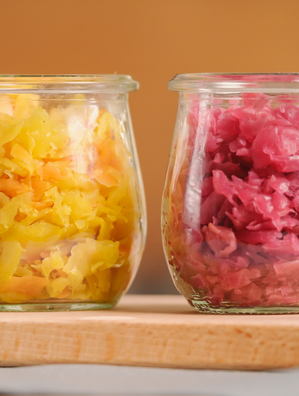 KI generiert: Zwei Gläser mit gelbem und pinkem fermentiertem Gemüse auf einem Holzbrett.