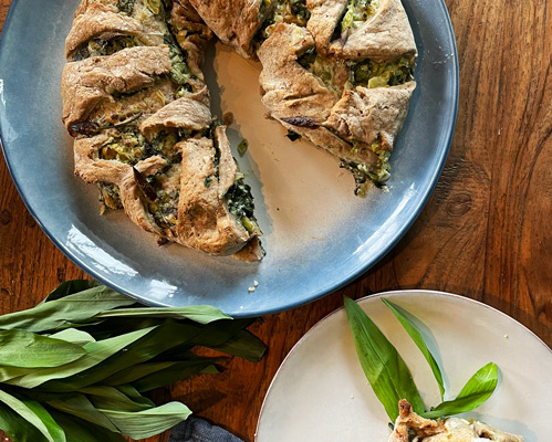 KI generiert: Herzhafte Tarte mit Kräutern auf einem Holztisch, daneben frische Kräuterblätter.