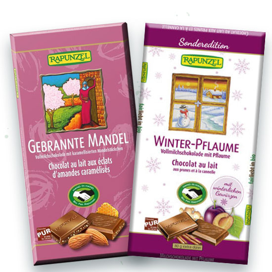 KI generiert: Das Bild zeigt zwei Tafeln Vollmilchschokolade der Marke Rapunzel. Die Geschmacksrichtungen sind "Gebrannte Mandel" und "Winter-Pflaume", letztere als Sonderedition.