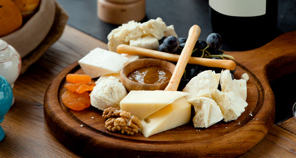 KI generiert: Eine Käseplatte mit verschiedenen Käsesorten, Nüssen, getrockneten Aprikosen und Trauben auf einem Holzbrett.