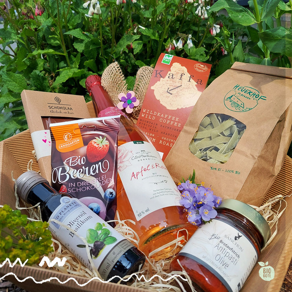 KI generiert: Geschenkkorb mit Bio-Produkten: Kaffee, Pasta, Öl, Schokolade, Früchte und ein Getränk, dekoriert mit Blumen.