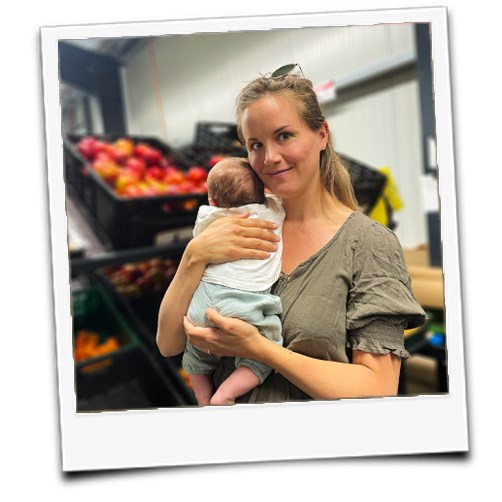 KI generiert: Eine Frau hält ein Baby; im Hintergrund sind Kisten mit Äpfeln.