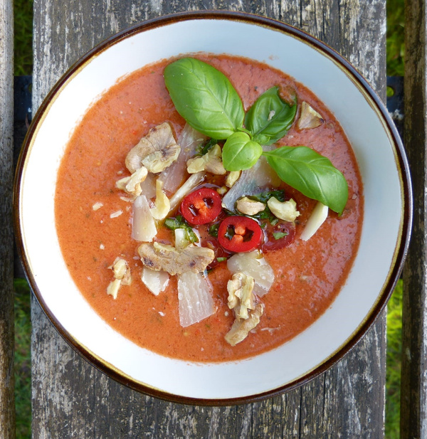 KI generiert: Ein Teller mit roter Suppe, garniert mit Basilikum, Nüssen und Chilis.