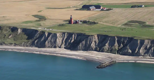 KI generiert: Küstenlandschaft mit Leuchtturm auf Klippe und umgebender Landwirtschaft.