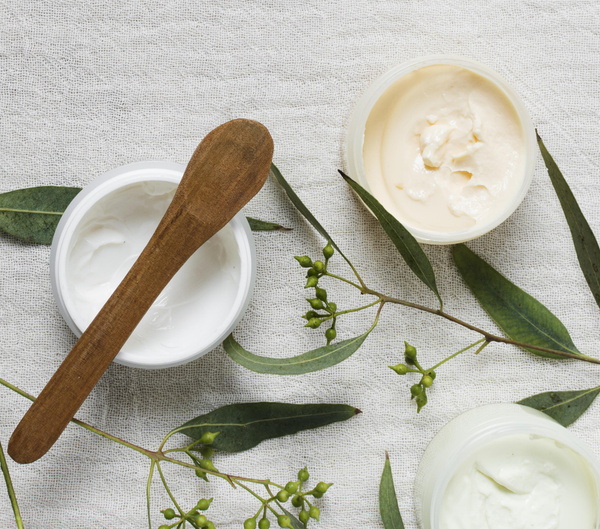 KI generiert: Kosmetikdosen mit Creme, Holzspatel und Eukalyptusblättern auf Leinenstoff.