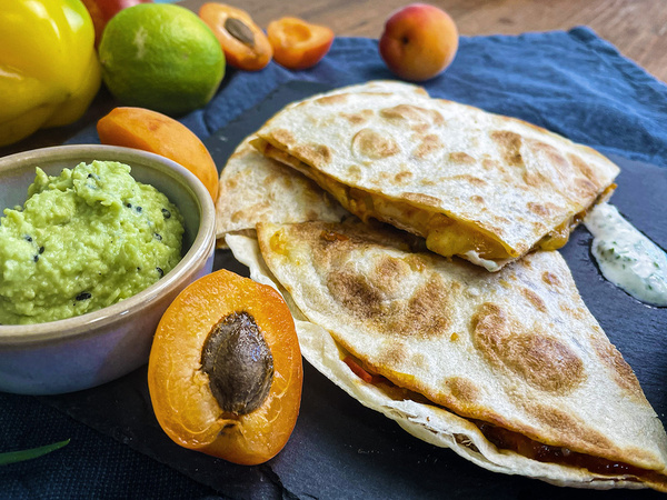 KI generiert: Quesadillas mit Guacamole und Aprikosen auf dunklem Untergrund.