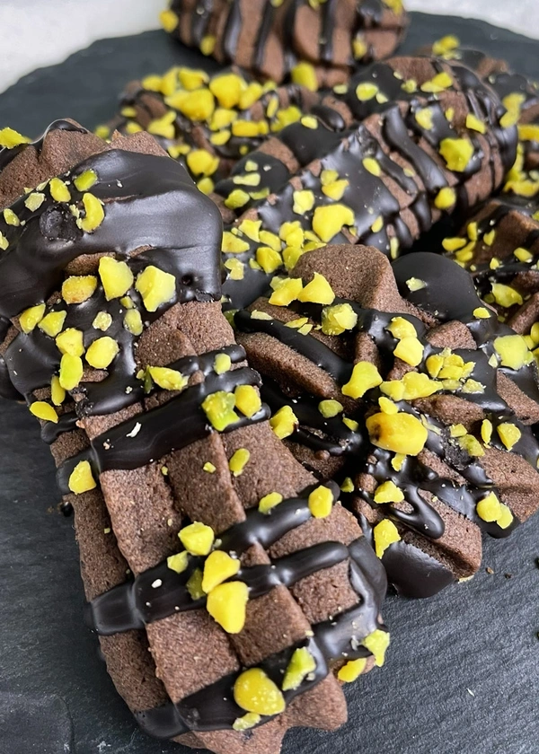 KI generiert: Kekse mit Schokoladenglasur und gehackten gelben Nüssen, auf einem dunklen Untergrund präsentiert.