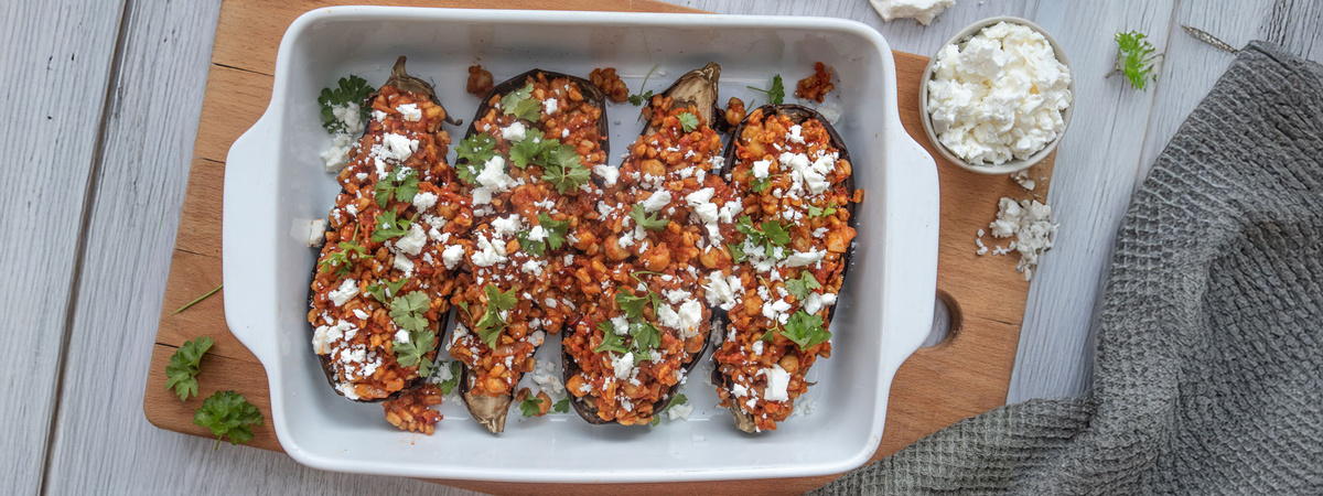 KI generiert: Gefüllte Auberginenhälften mit einer Mischung aus Linsen und Käse in einer weißen Auflaufform, garniert mit Kräutern.