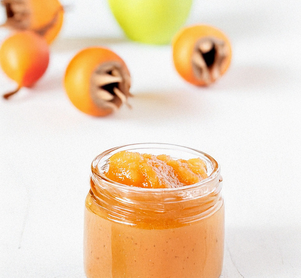 KI generiert: Ein Glas mit gelber Marmelade, umgeben von reifen Früchten auf weißem Hintergrund.