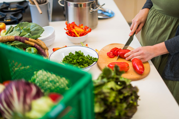 schwangere frau schneidet Tomaten auf einem Schneidebrett in der Küche. Frisches Gemüse ist auf dem Tisch.