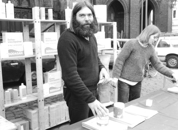 KI generiert: Ein Mann und eine Frau präsentieren Produkte an einem Stand. Text: "SODASAN Seifenwaschpulver".