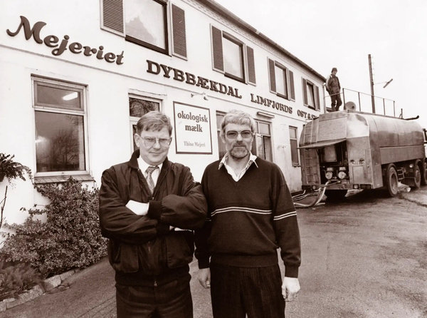 KI generiert: Zwei Männer vor einer Molkerei. Text: "Mejeriet Dybækdal", "økologisk mælk", "Thise Mejeri".