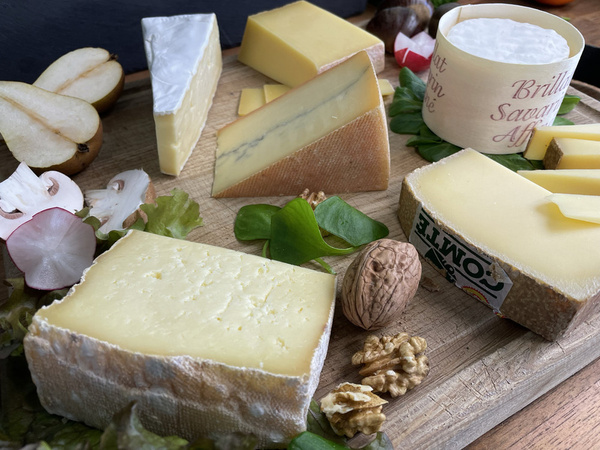 KI generiert: Verschiedene Käsesorten auf einem Holzbrett, umgeben von Nüssen und Obst.