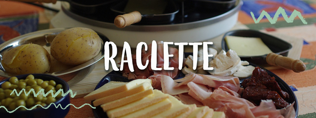 Das Bild zeigt verschiedene Zutaten, die typischerweise beim Raclette verwendet werden, wie Kartoffeln, Schinken, Käse und eingelegte Tomaten. Im Hintergrund ist ein Raclette-Grill zu sehen.