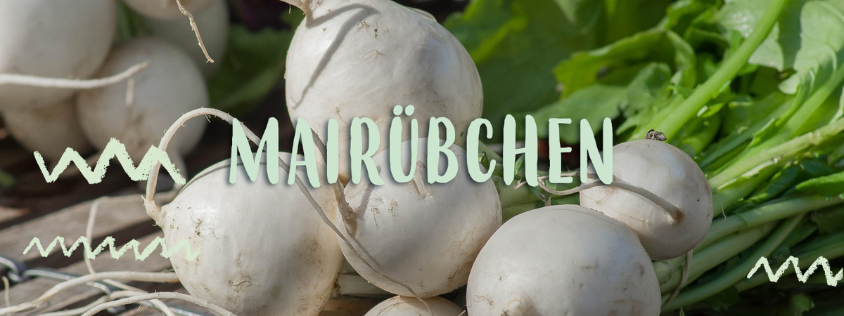 KI generiert: Mairübchen liegen auf einer Oberfläche, umgeben von grünen Blättern. Text: "MAIRÜBCHEN".