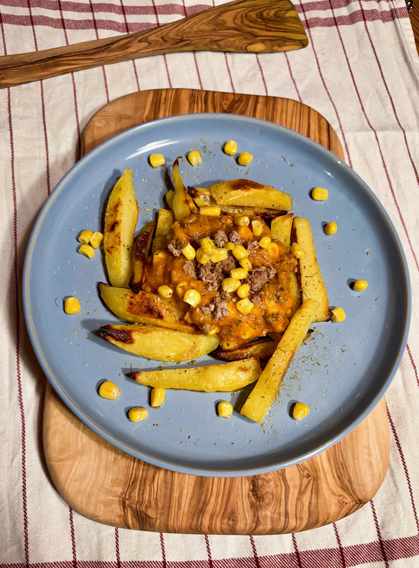 KI generiert: Gericht mit Kartoffelecken, Käse, Hackfleisch und Mais auf einem blauen Teller.