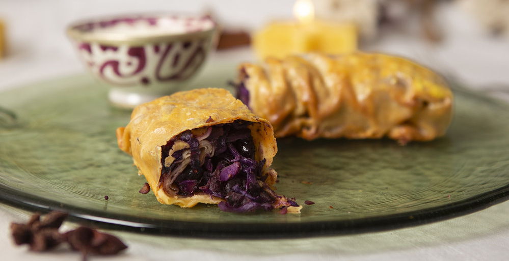 KI generiert: Ein Strudel mit Rotkrautfüllung auf einem Teller. Im Hintergrund ein verzierter Becher.