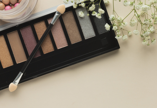 KI generiert: Lidschattenpalette mit verschiedenen Erdtönen und Applikator, daneben weiße Blumen.
