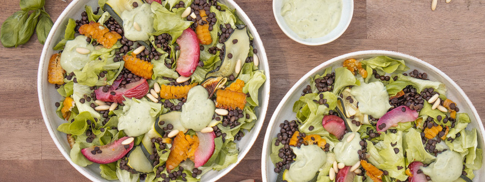 KI generiert: Zwei Schüsseln mit buntem Salat, Linsen, Kürbis, Radieschen und grüner Soße.