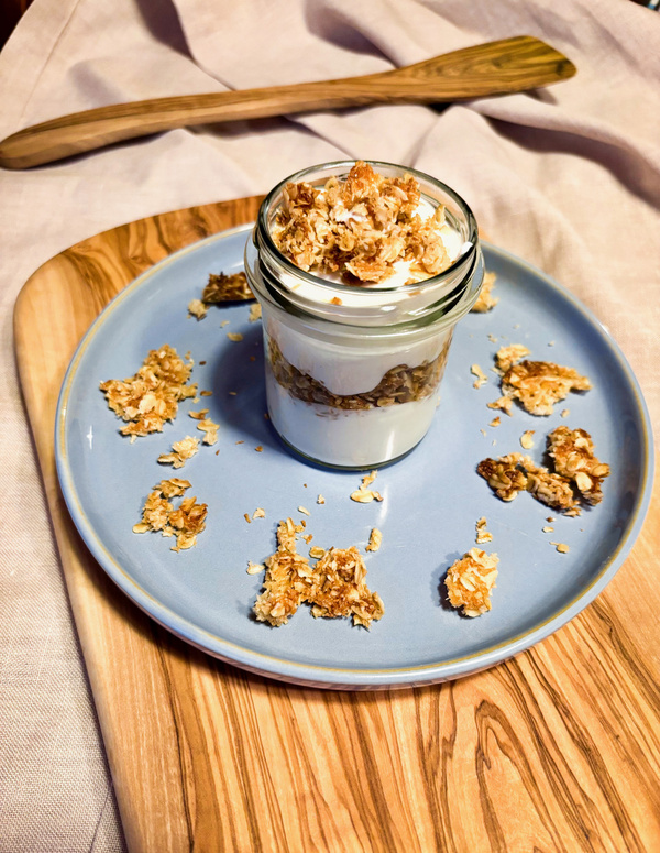 KI generiert: Ein Dessertglas mit Joghurt und Müsli auf einem blauen Teller, garniert mit knusprigen Flocken.