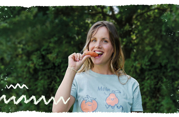 KI generiert: Eine Person isst eine Karotte und trägt ein hellblaues T-Shirt mit einem Cartoon-Motiv darauf. Der Hintergrund ist grün und leicht verschwommen, vermutlich eine Außenaufnahme.