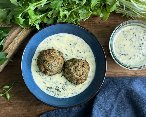 KI generiert: Zwei herzhafte Knödel in einer cremigen Sauce in einer Schüssel, mit frischem Grün im Hintergrund.