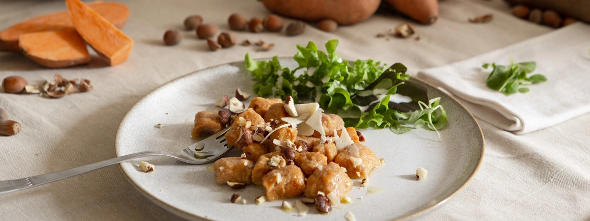 KI generiert: Ein Teller mit Süßkartoffel-Gnocchi, Salat und gehackten Nüssen auf einem Tisch.