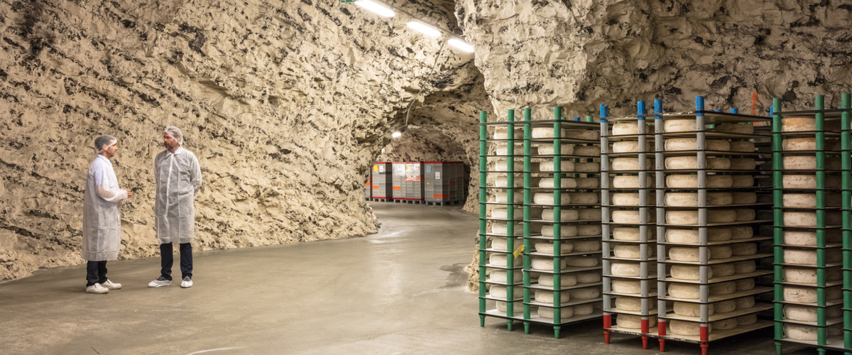 KI generiert: Einige Menschen stehen in einem Tunnel neben gestapelten Kisten in einem natürlichen, steinernen Lagerraum.