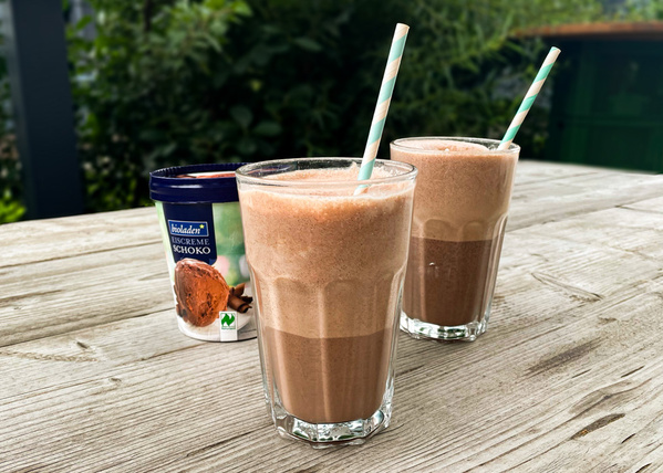 KI generiert: Zwei Gläser mit Schokoladenshake und Papierzuckern auf Holztisch. Text: "bioladen * EISCREME SCHOKO".
