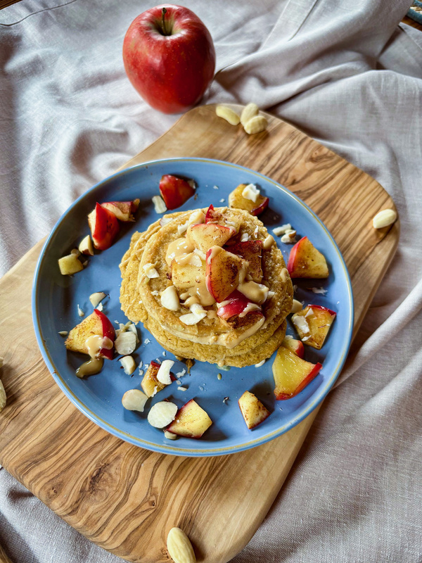 KI generiert: Pfannkuchen mit Äpfeln und Mandeln auf einem blauen Teller; ein Apfel daneben.
